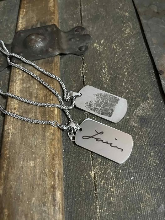 Two engraved metal tags on chains with a fingerprint and signature