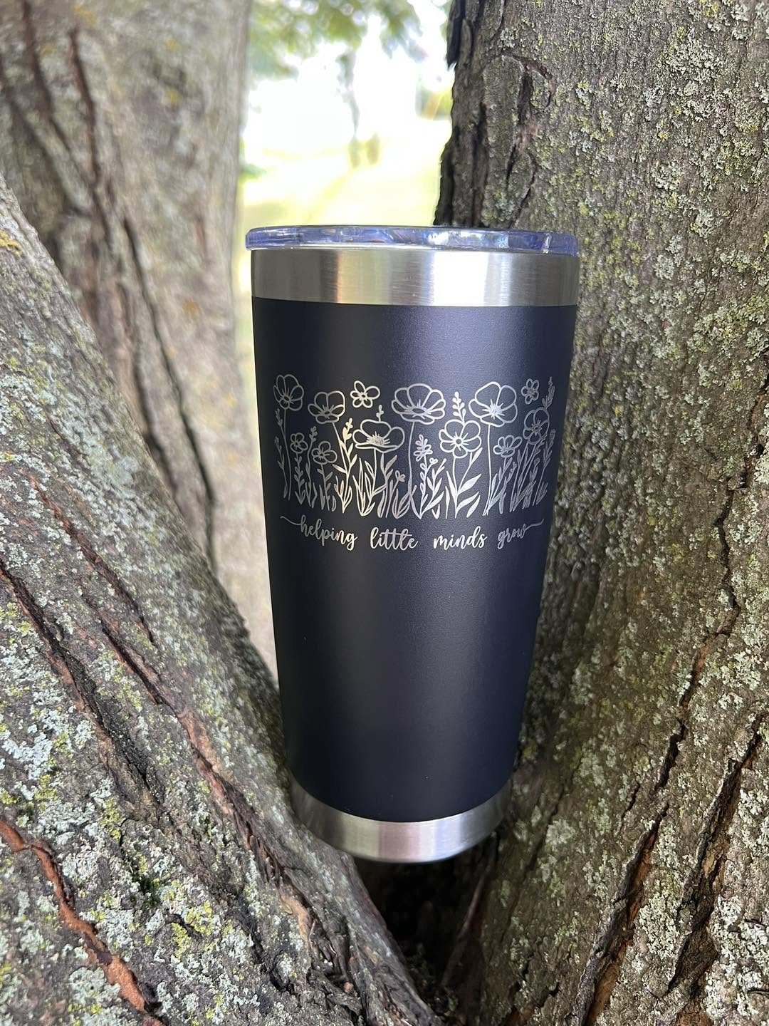 Black tumbler engraved with floral artwork and helping little minds grow text