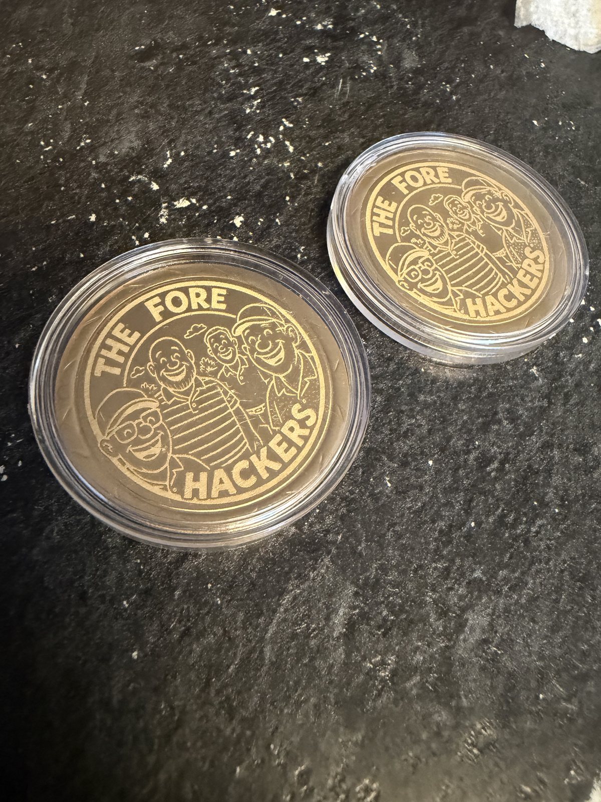 Gold-toned challenge coins engraved with The Fore Hackers artwork